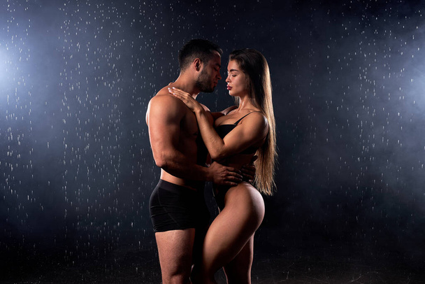Portrait of passionate beautiful couple posing hugging under heavy rain on black background - Zdjęcie, obraz