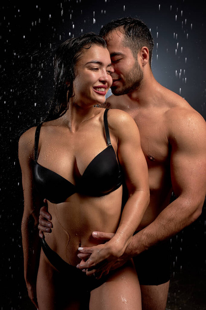 athletic wet passionate romantic couple hugging in water drops on black background - Fotó, kép