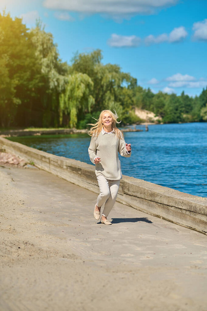 Smiling woman in casual clothes running near sea - Photo, Image