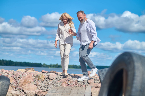 Man and woman walking on stones near sea - Foto, imagen