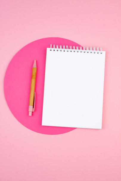 Notepad and pen on a pink background in a flat lay style with a paper crimson circle on the background. Planning concept for 2022. - Foto, Imagem