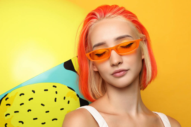 Beautiful young woman with bright dyed hair and inflatable ball on orange background - Foto, Imagem