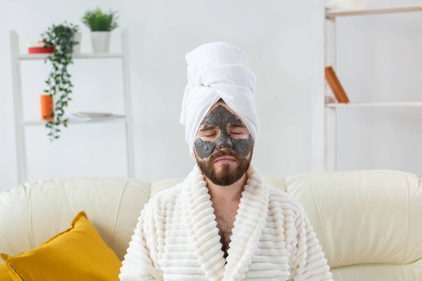 Bearded man has clean fresh skin, wears beauty clay mask on face and enjoys beauty treatments. Spa at home, body and skin care - Fotografie, Obrázek