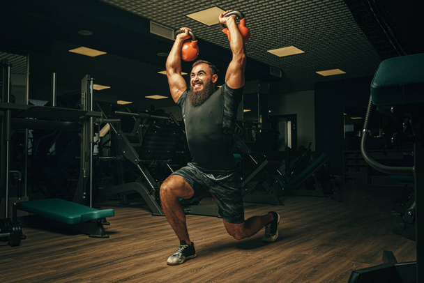 Bodybuilder κάνει ασκήσεις με αλτήρες σε ένα σκοτεινό γυμναστήριο - Φωτογραφία, εικόνα