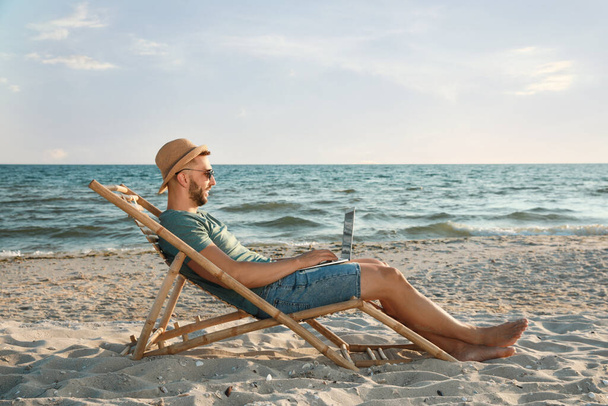 Man working with laptop in deck chair on beach - Foto, Imagen