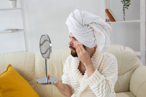 Красивый мужчина чистит кожу лица хлопчатобумажными прокладками и смотрит в зеркало. Спа, уход за телом и кожей для мужской концепции. - Фото, изображение