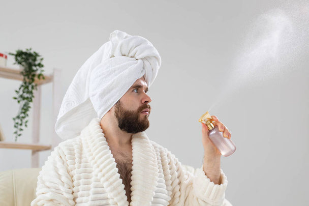 Homem barbudo com toalha de banho na cabeça aplicando tratamento de água spray no rosto. Spa, corpo e cuidados com a pele para o conceito de homem. - Foto, Imagem