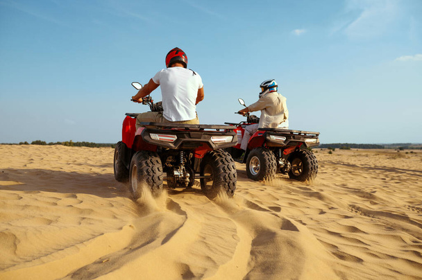 Δύο άνδρες με κράνη ιππεύουν στο Atv στην άμμο της ερήμου - Φωτογραφία, εικόνα