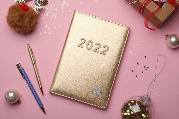 Golden planner with number 2022, stationery and festive decor on pink background, flat lay. New Year aims - Fotó, kép