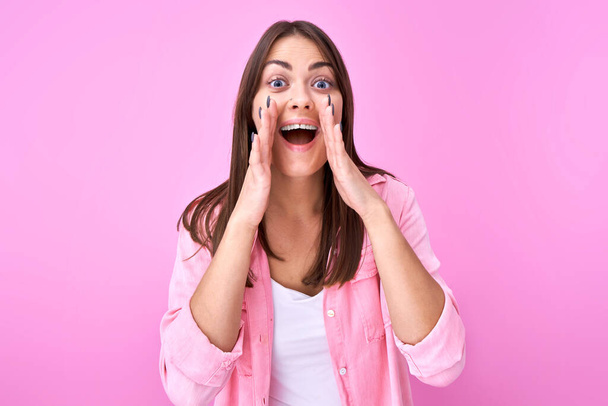 Young happy brunette girl shouting and cupping hands around mouth isolated on pink studio background. Excited news attention! - Foto, Imagem