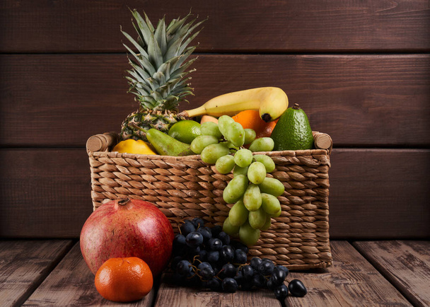 Mix of fresh juicy colorful exotic tropical fruits in basket on wooden background - Fotografie, Obrázek