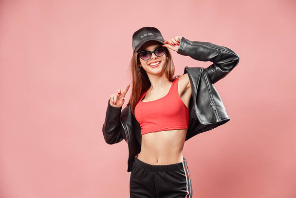 nice looking teenage girl in glasses in black cap gestures hands while isolated over pink background - 写真・画像