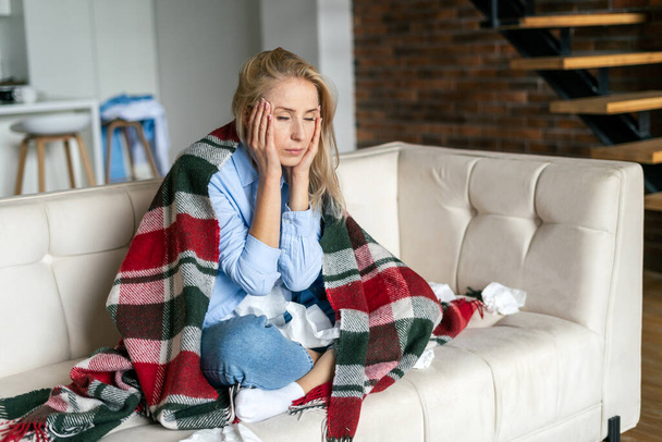 Sick woman feel pain, having terrible strong headache. Tired and upset female massaging temples, suffering from migraine, spending day at home, sitting on couch, wrapped in plaid - Foto, immagini