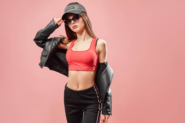 nice looking teenage girl in sunglasses in black cap posing while isolated over pink background - Photo, image