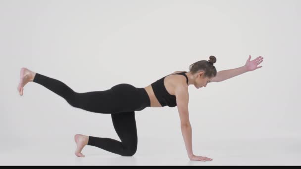 Jovem mulher esportiva ajoelhada no chão e praticando postura de alongamento nas costas, levantando a perna e a mão e curling corpo - Filmagem, Vídeo