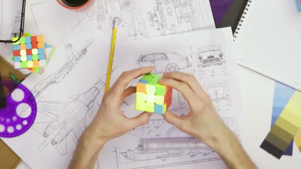 Κορυφή δείτε τα χέρια ενός άνδρα σχεδιαστή λύσει ένα παζλ με ένα κύβο Rubiks. Κύβος παζλ, ένα παιχνίδι παζλ. - Πλάνα, βίντεο