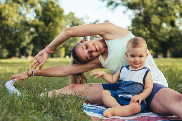 mother does physical exercises with her baby boy in park - Photo, Image