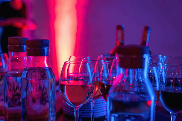 Glasses of wine and snacks on a bar table in night club blue and red neon lights. Party or nightlife entertainment with copy space - Foto, imagen