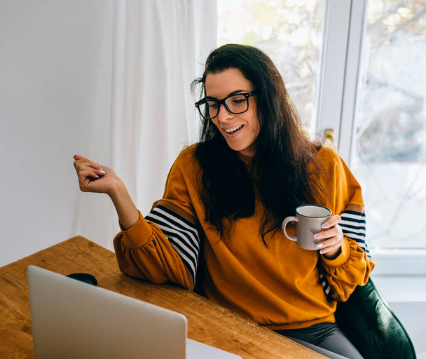 Uśmiechnięta kobieta w swoim biurze ma wideo połączenie na komputerze. Pracownica niezależna i pracująca zdalnie w domu. Mama blogger za pomocą sklepu internetowego. - Zdjęcie, obraz