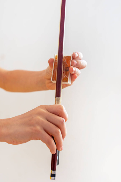 manos de un joven violinista colofonia su arco sobre un fondo claro, vertical - Foto, Imagen