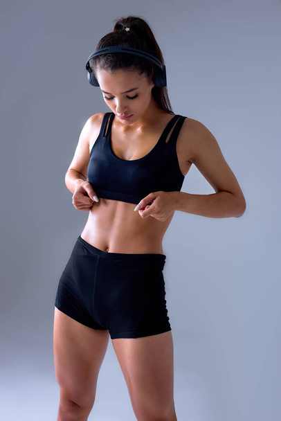 Confident sportswoman showing press cubes without fat on body in black top tracksuit. - Fotó, kép