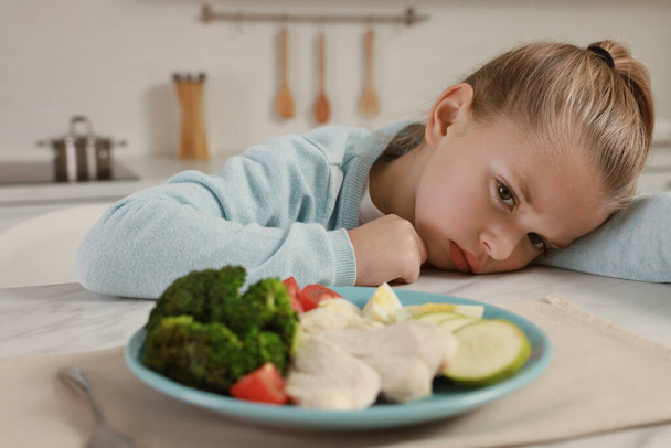 Cute little girl refusing to eat dinner in kitchen - Fotografie, Obrázek