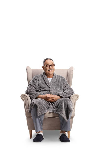 Mature man in a bathrobe and pajamas sitting in an armchair isolated on white background - Photo, Image