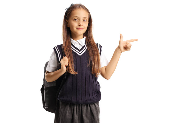 Girl in a school uniform with a backpack pointing to the side isolated on white background - Photo, Image