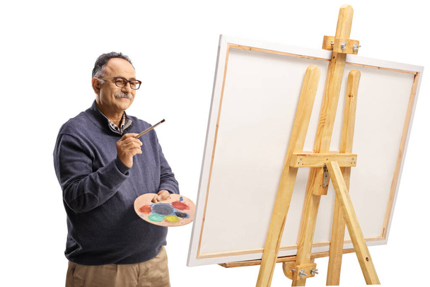 Mature man with a brush and palette painting on a canvas isolated on white background - Fotoğraf, Görsel
