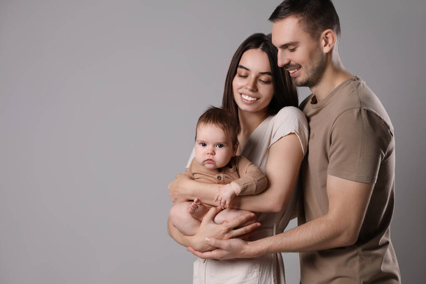 Happy family. Couple with their cute baby on grey background, space for text - Foto, afbeelding