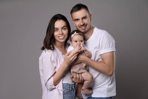 Happy family. Couple with their cute baby on grey background - Φωτογραφία, εικόνα