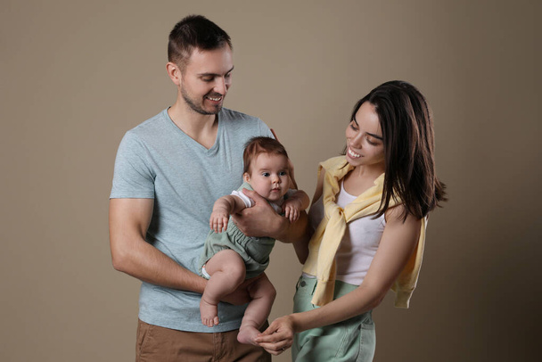 Happy family. Couple with their cute baby on beige background - Zdjęcie, obraz