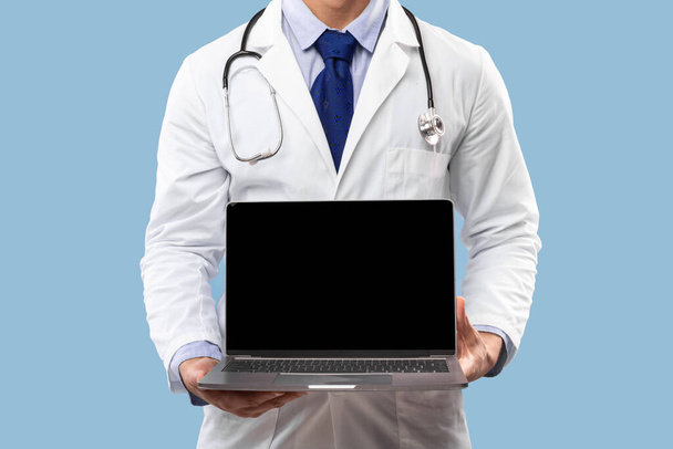 Arabic Male Doctor Showing Blank Laptop Over Blue Background, Cropped - 写真・画像