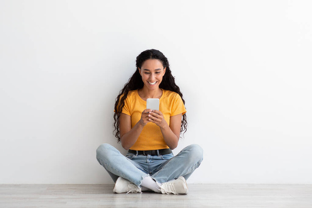 Portrait Of Excited Young Brunette Woman With Smartphone Sitting On Floor - Valokuva, kuva
