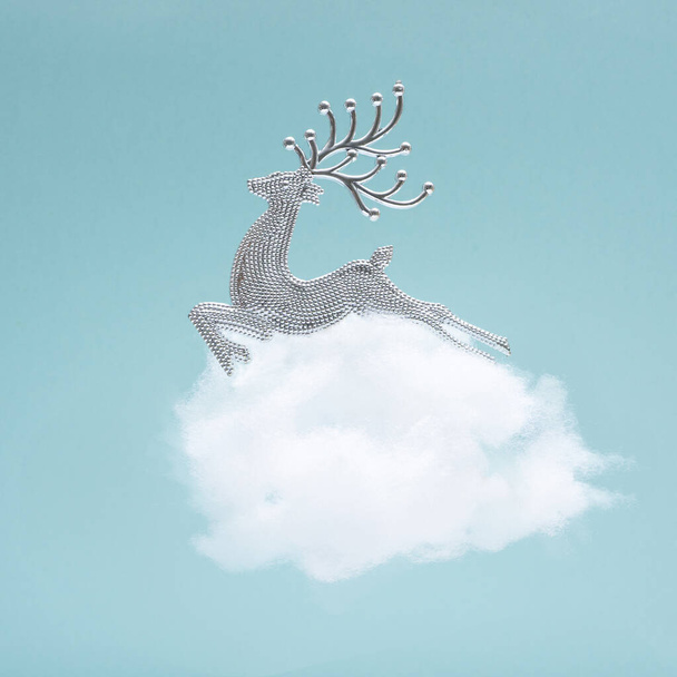 Inspired by new year coming. Shiny silver reindeer ornament at top of cloud with polar blue background - Photo, Image