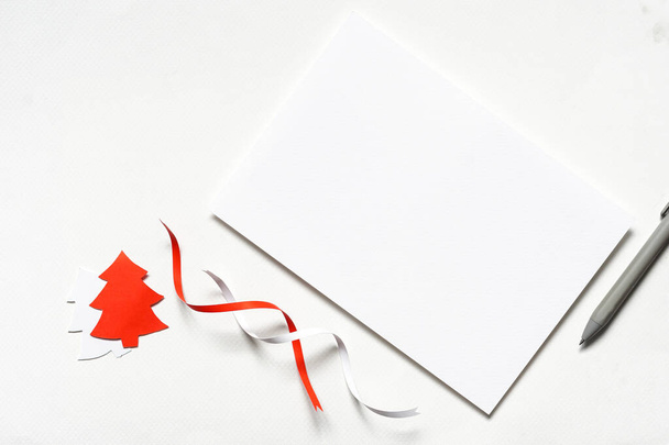 Biała kartka okolicznościowa z czerwoną białą wstążką, papierem w kształcie choinki i szarym długopisem na białym papierze - Zdjęcie, obraz