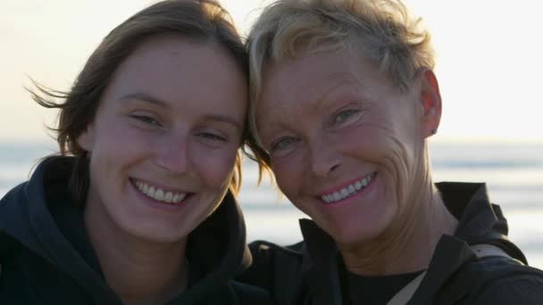 Matka a dcera se usmívají na kameru, užívají si pláž při západu slunce - Záběry, video