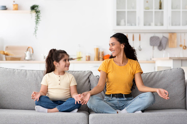 Aranyos kislány és a fiatal anyja együtt meditálnak otthon. - Fotó, kép