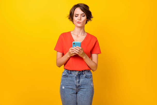 Photo of nice brunette sad lady look telephone wear red t-shirt isolated on vivid yellow color background - Fotoğraf, Görsel