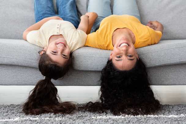 Cheerful Funny Young Mother And Little Daughter Lying On Couch Upside Down - Фото, изображение