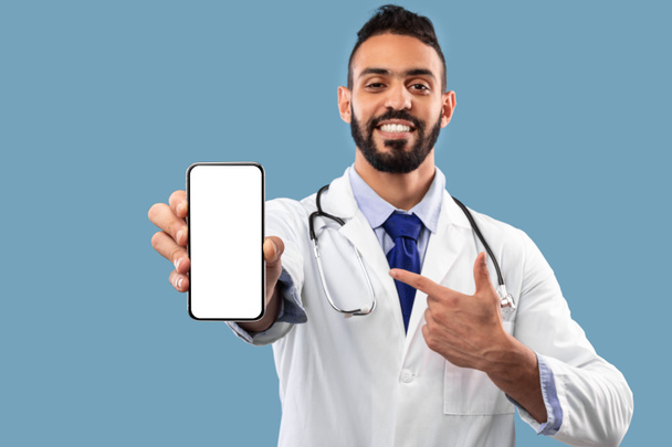 Ближневосточный доктор показывает пустой экран мобильного телефона на синем фоне - Фото, изображение