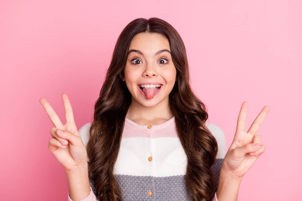 Photo of young school girl happy smile grimace fooling tongue-out show peace cool v-sign isolated over pastel color background - Photo, Image