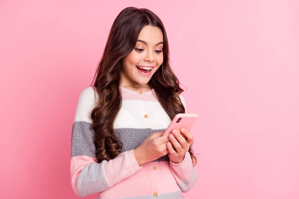 Photo of brunette wavy haired little girl look read message phone amazed news isolated on pink color background - Фото, зображення