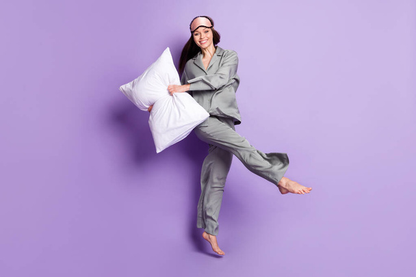 Full length body size photo of pretty woman in grey sleepwear dancing with pillow smiling isolated pastel violet color background - Foto, afbeelding