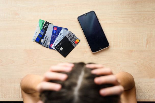ロシアのウラジーミル- 10月2021: 1人の男がプラスチック製の銀行カードの山の上に頭を保持します。借金の概念. - 写真・画像