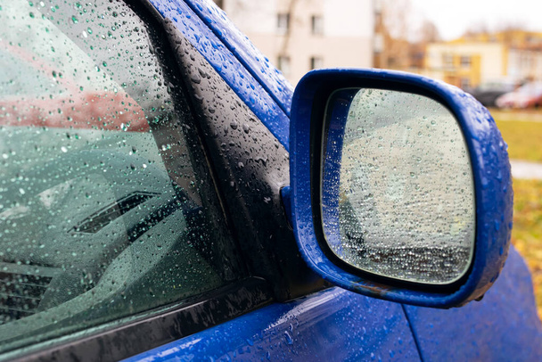Σταγόνες βροχής στον πλευρικό καθρέφτη ενός μπλε αυτοκινήτου από κοντά - Φωτογραφία, εικόνα