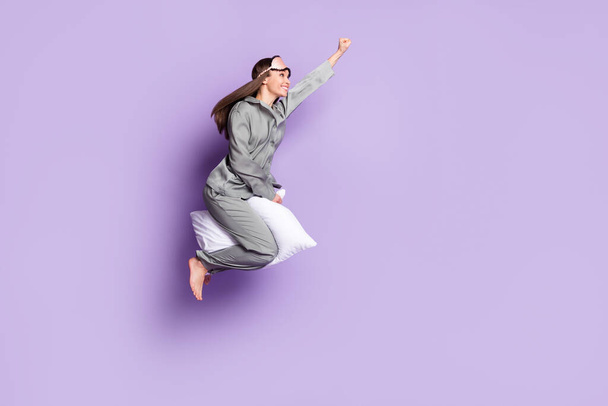 Full length body size photo of super woman riding on pillow flying high looking copyspace isolated pastel violet color background - Фото, изображение