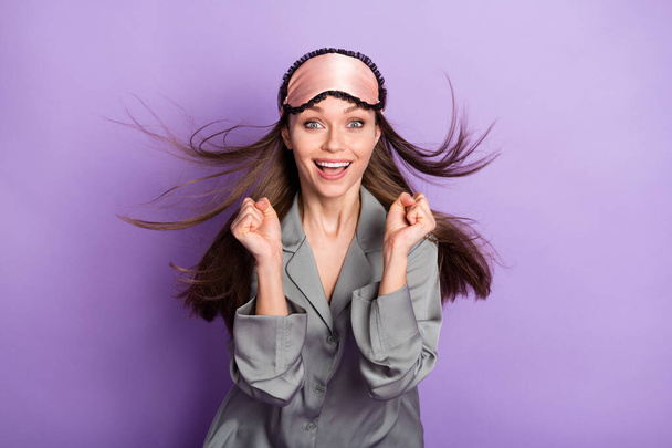 Photo portrait of pretty girl in grey pajama sleeping mask smiling gesturing like winner isolated pastel violet color background - Foto, afbeelding