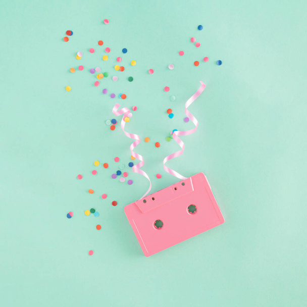 Creative arrangement made of vintage pink cassette tape, confetti and decorative ribbons on a mint green background.. Minimal retro music concept. Party and celebration inspiration. - Photo, Image