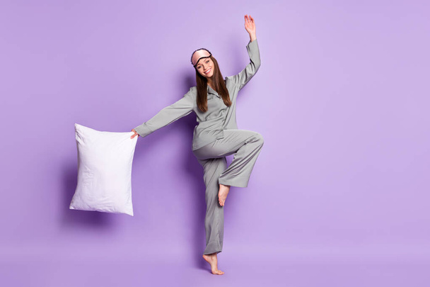 Full length body size view of lovely cheerful girl wear pajama carrying pillow jumping having fun isolated on violet purple color background - Zdjęcie, obraz